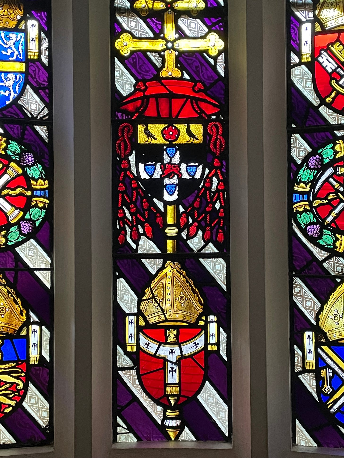 Stained glass window featuring a cardinal’s hat and Wolsey’s arms with Cornish Choughs, lions and a Tudor rose. The stained glass is highly coloured. 