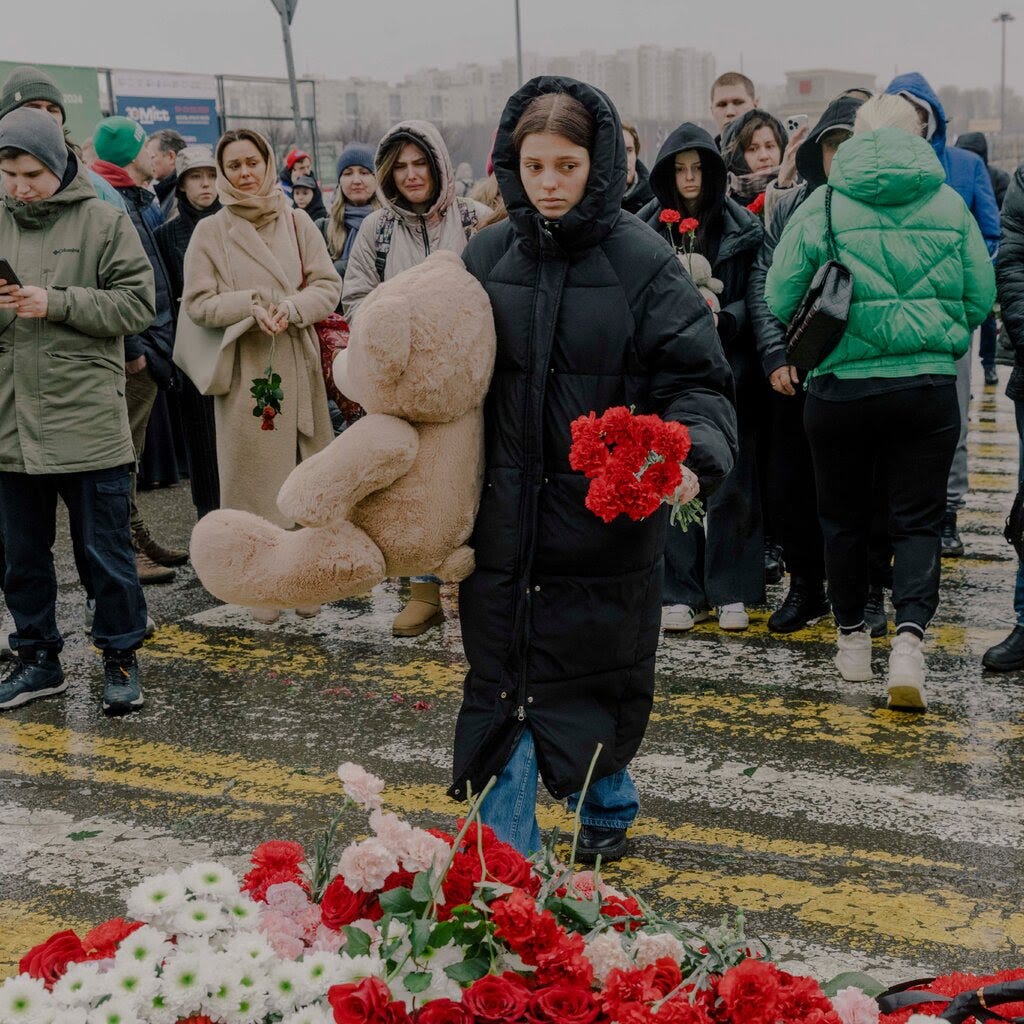 Mourners on a street in Moscow. A woman holds flowers in one hand and a teddy bear in the other. 