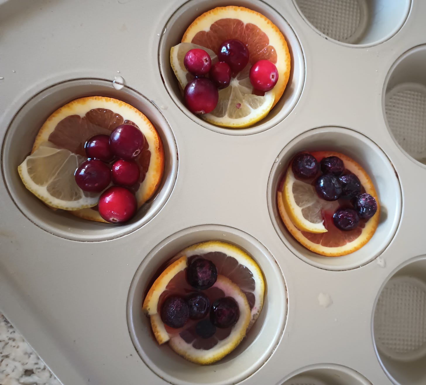 muffin tins with orange and lemon slices, cranberries and blueberries