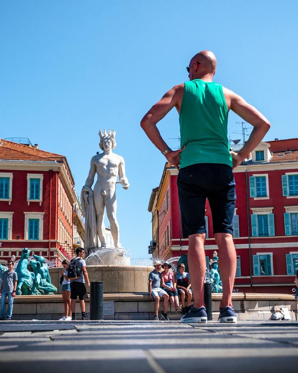 man in teal tank top and black shorts standing in front of statue