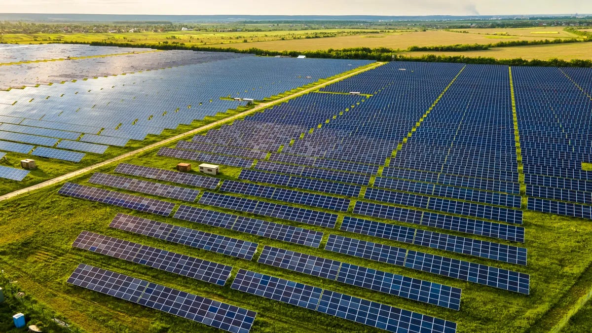 An aerial view of a solar power plant with many rows of solar photovoltaic panels.