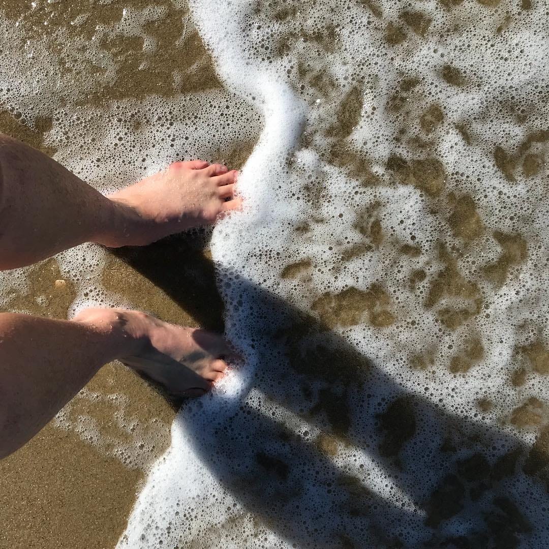 My feet in the foamy white surf on a beach.