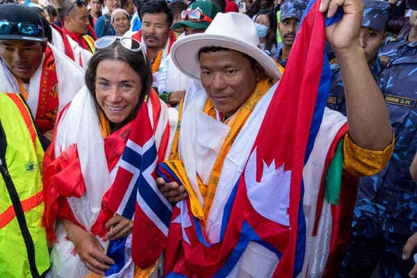 Kristin Harila, wrapped in a Norwegian flag, stands with a man, Tenjen Sherpa, her mountain guide