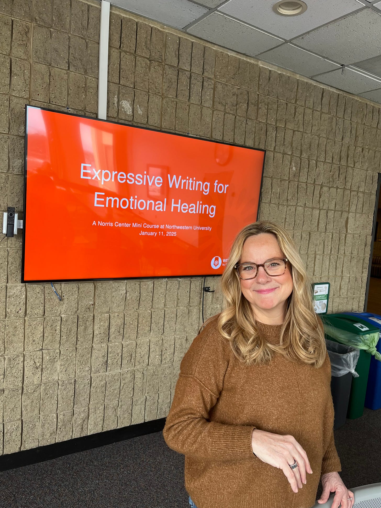 blonde woman standing in front of tv monitor with orange background and words that say "Expressive Writing for Emotional Healing"