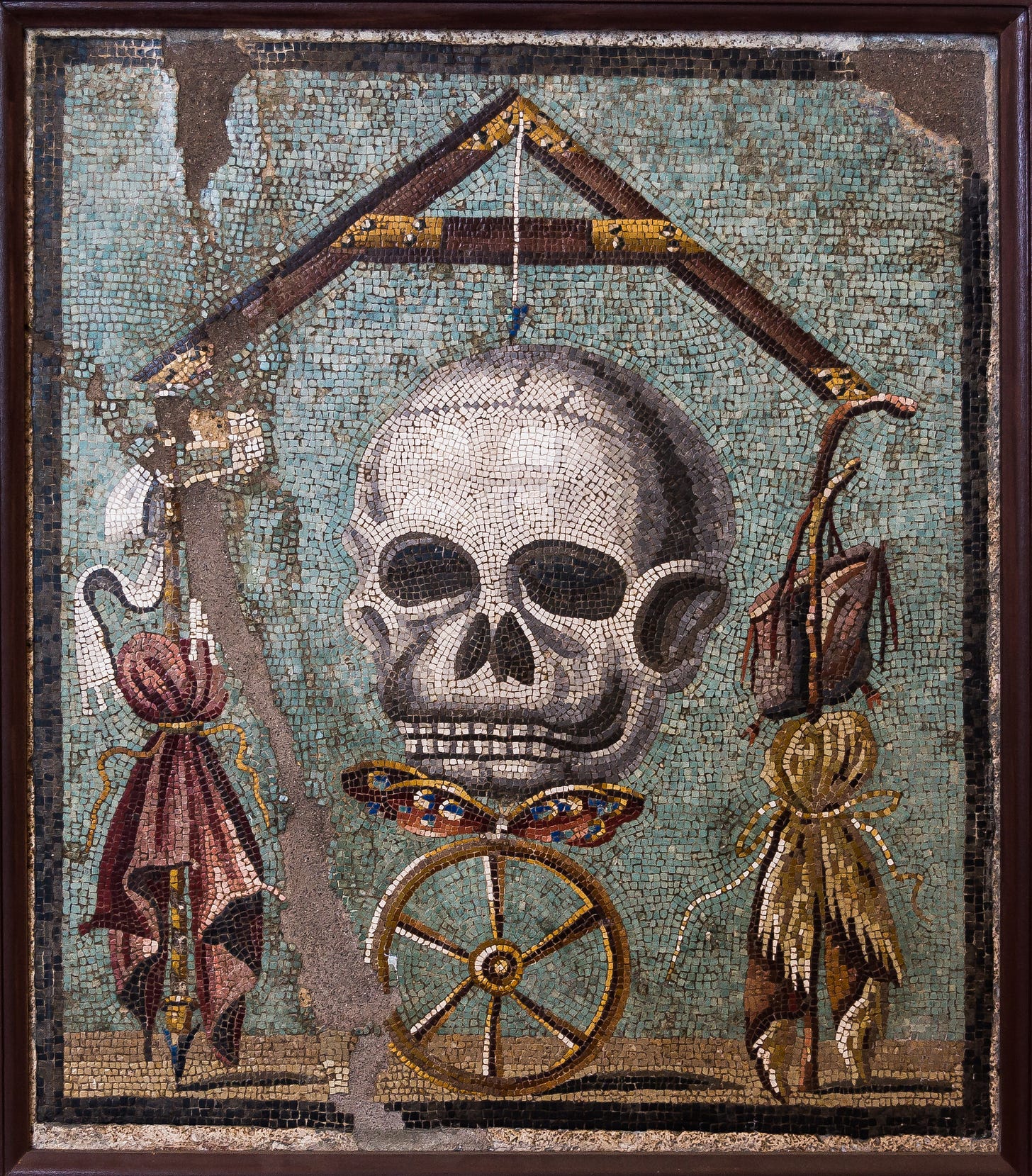 A mosaic of a skull from a frieze recovered from the Pompeii volcano eruption. The weight is death (the skull) below which are a butterfly (the soul) and a wheel (fortune). On each side, suspended from the arms of the level and kept in perfect balance by death, are the symbols of wealth and power on the left (the sceptre and purple) and poverty on the right (the beggar’s scrip and stick). The theme, like the skeletons on the silverware in the treasure of Boscoreale, was intended to remind diners of the fleeting nature of earthly fortunes.