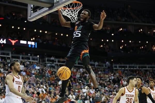 Miami’s Wooga Poplar, in a No. 55 jersey with “U” written on it, dunks the ball, with Texas defenders below him.