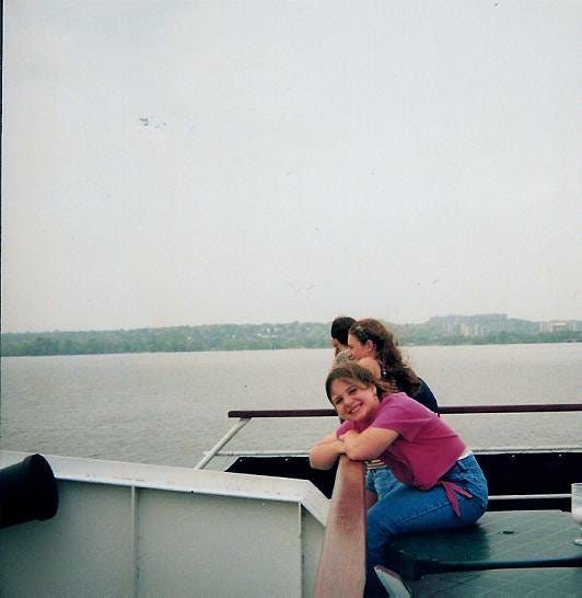 The author is pictured here as a child, wearing blue jeans and a pink shirt. She is around 7-9 years old and is perched with her elbows on the railing of a boat as she looks and smiles at the camera. A river and land are in the distance -- I'm pretty sure this was taken on a cruise on the Potomac River touring Washington, D.C.