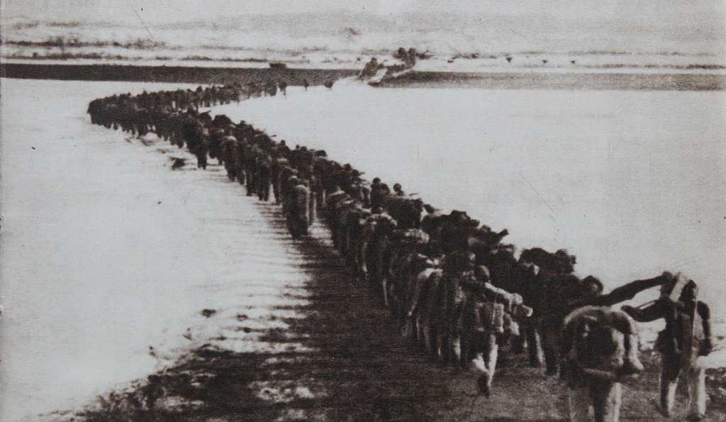 Ground level photo in black and white showing a long line of Chinese troops in several columns crossing the frozen Yalu river entering North Korea. The soldiers are dressed in quilted clothing and carrying their weapons. There are no trucks or other support equipment in the photograph. Ground level photo in black and white showing a long line of Chinese troops in several columns crossing the frozen Yalu river entering North Korea. The soldiers are dressed in quilted clothing and carrying their weapons. There are no trucks or other support equipment in the photograph.