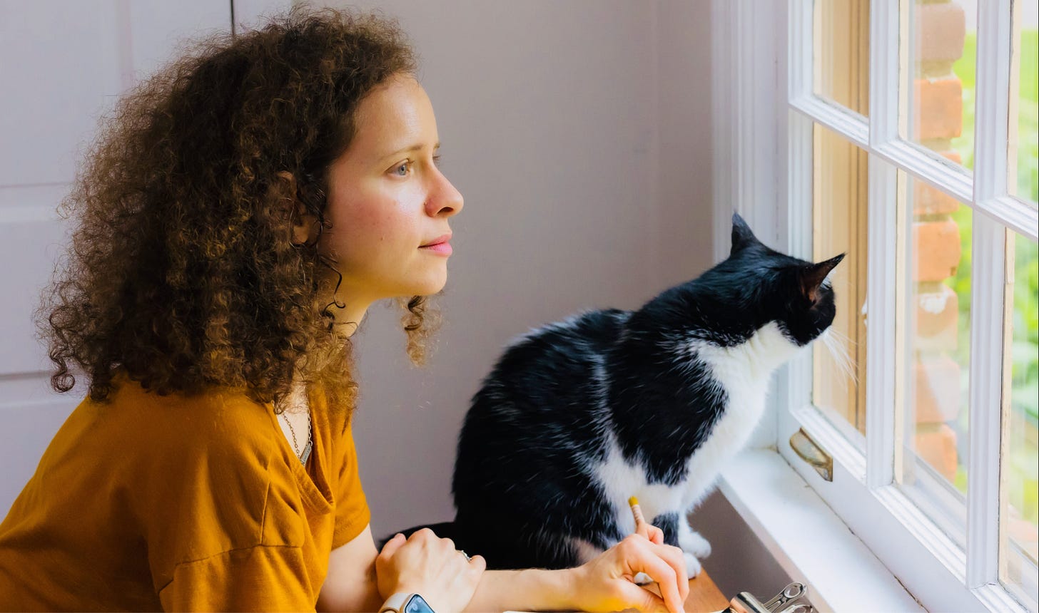 Beth Spencer and her black and white cat, looking out a window together