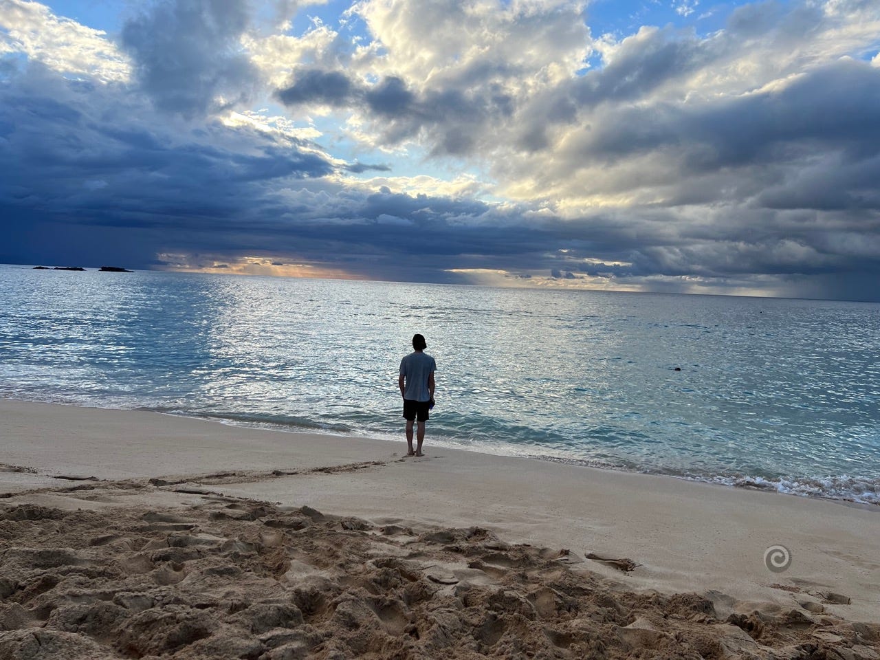 A young man stands alone at the water's edge. It's the beach at Waimea Bay on Oahu at sunset. A storm can be seen at the distance. There's a story in this picture, the topic of this article from Projectkin.org