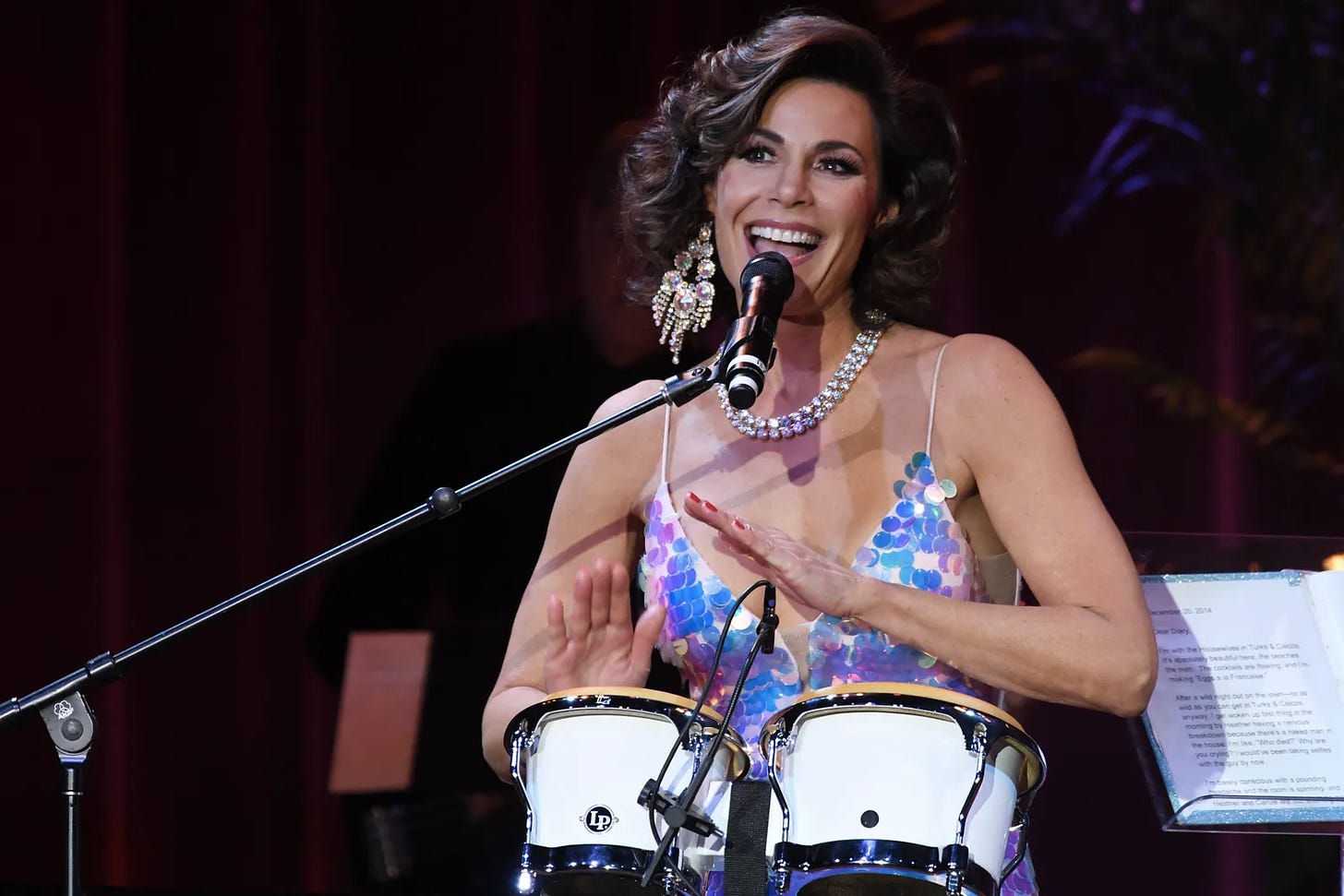 Luann de Lesseps plays the drums and talks into a microphone on stage during her cabaret show