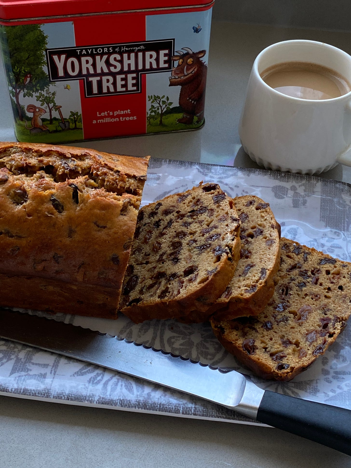 Fruit Tea loaf with slices cut out. A tin of tea and a cup in the background.