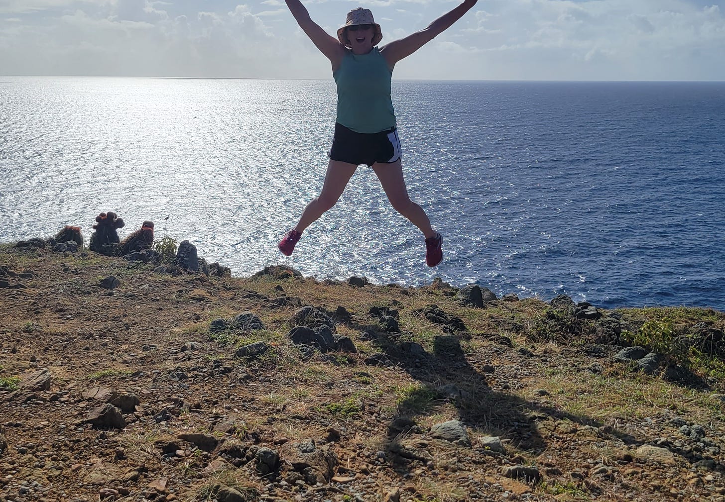 Catherine H Palmer writer jumps with joy overlooking the Caribbean ocean on Ram's Head, St. John USVI