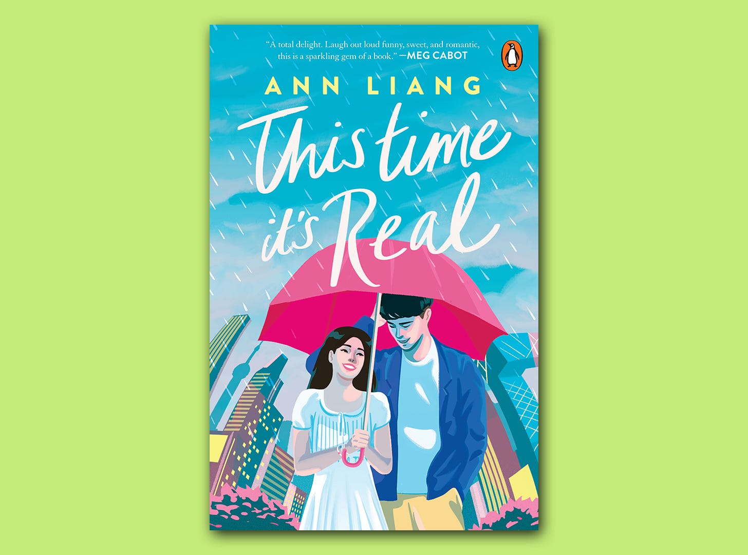The book cover for 'This Time it's Real' superimposed on a light green colour block background. The book cover shows an illustration of a boy and a girl sharing a pink umbrella under a light rain shower.