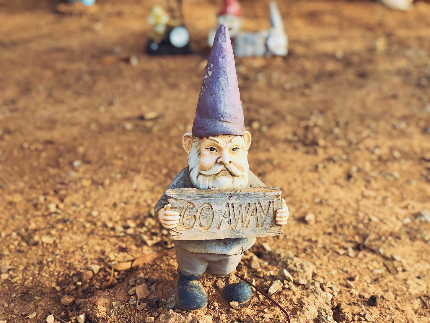 A small garden gnome holding a sign that says "go away!".