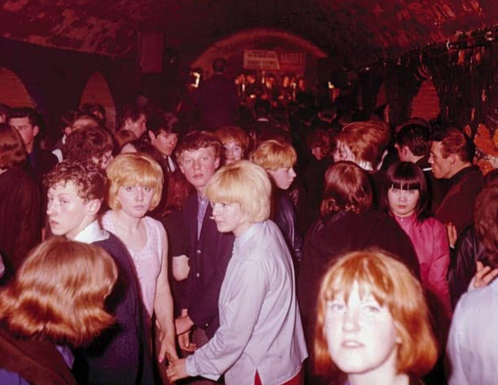 Crowd inside the Cavern Club. Mostly young people looking a bit sweaty, aware of the camera and looking at it, but not doing anything outlandish and not dressed outlandish in any way. Just a normal night at a club.
