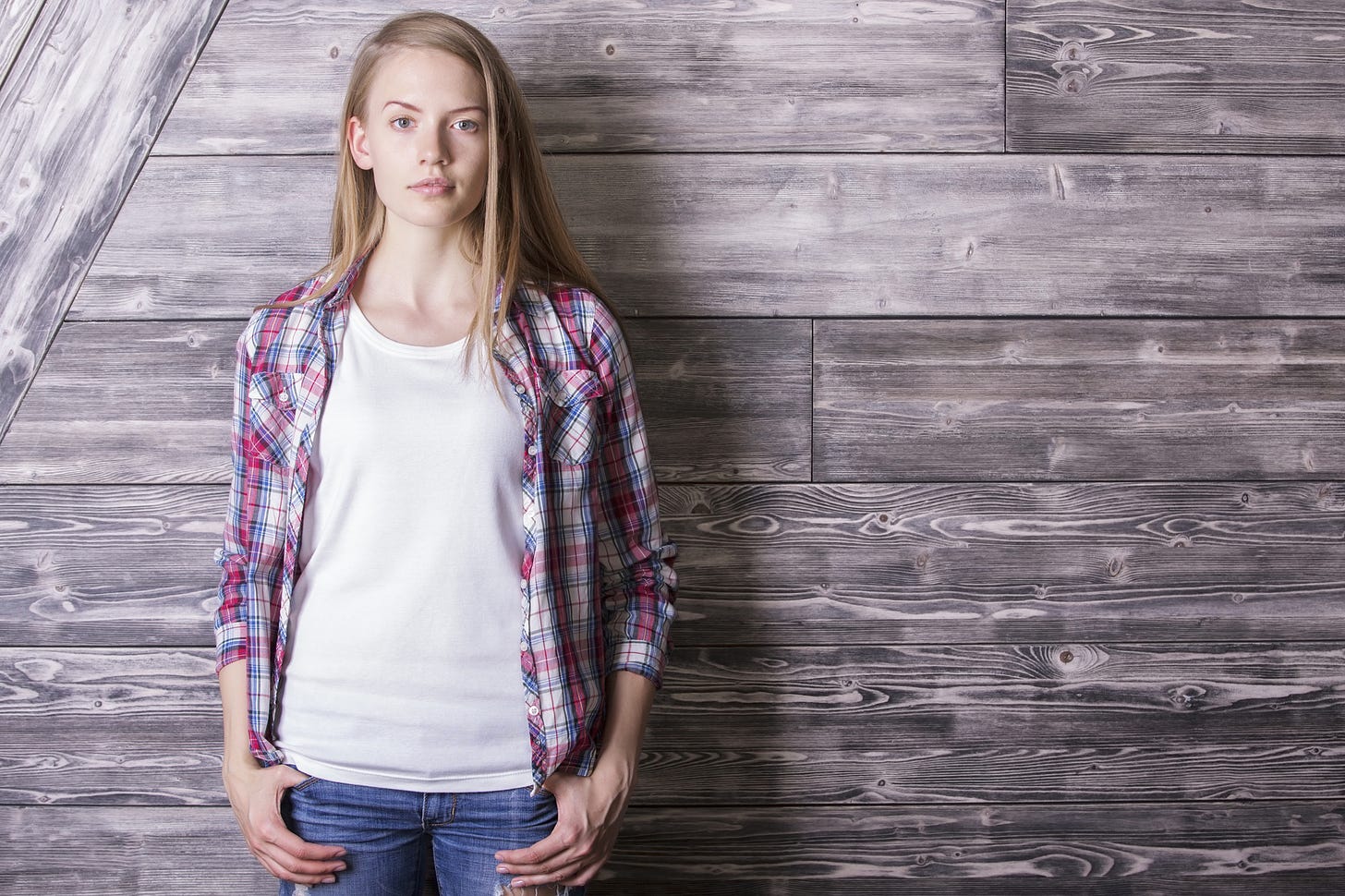 Young, casually dressed woman looking directly to camera, standing in front of a wooden wall