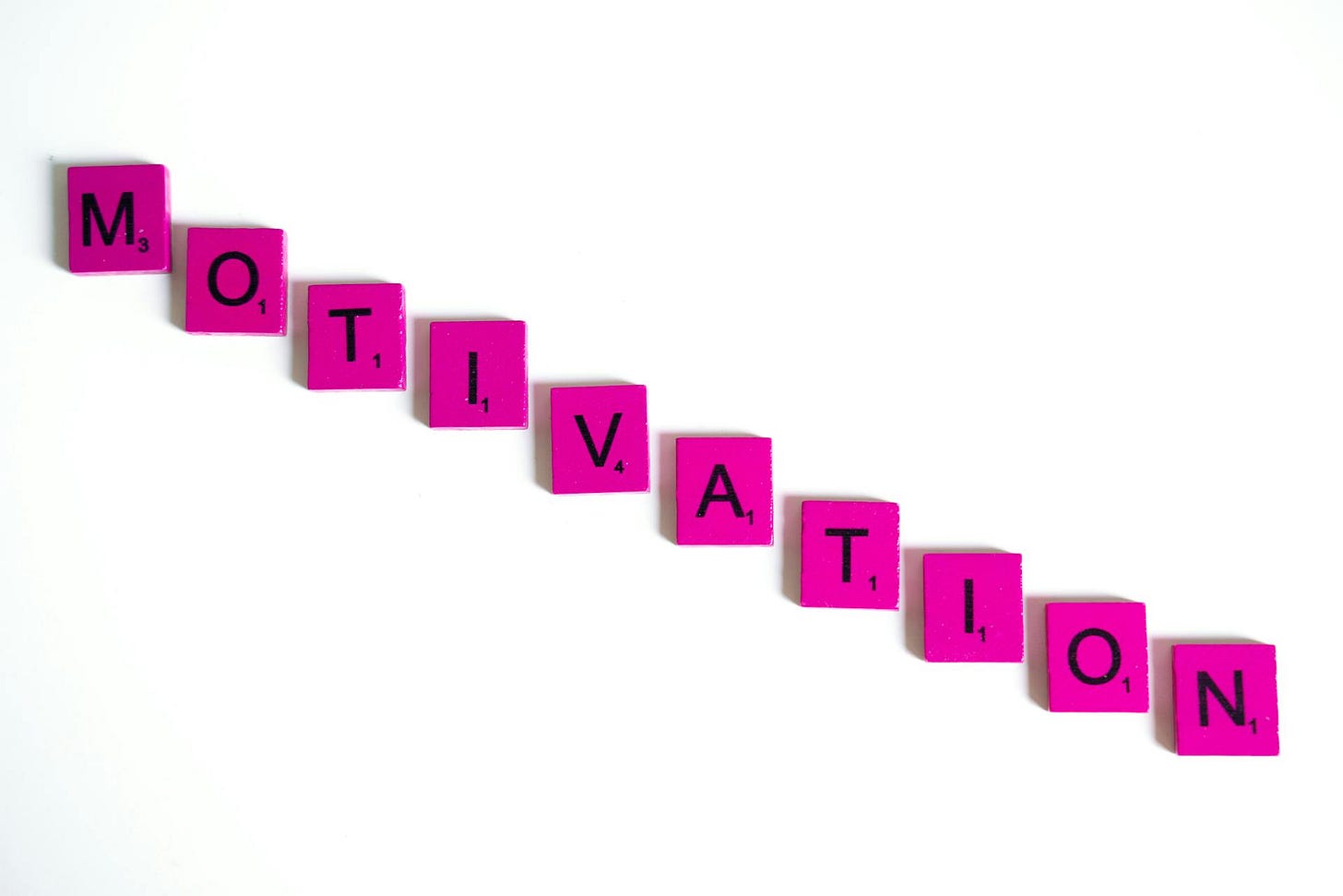 Pink Scrabble tiles on a white background spelling out the word "Motivation"