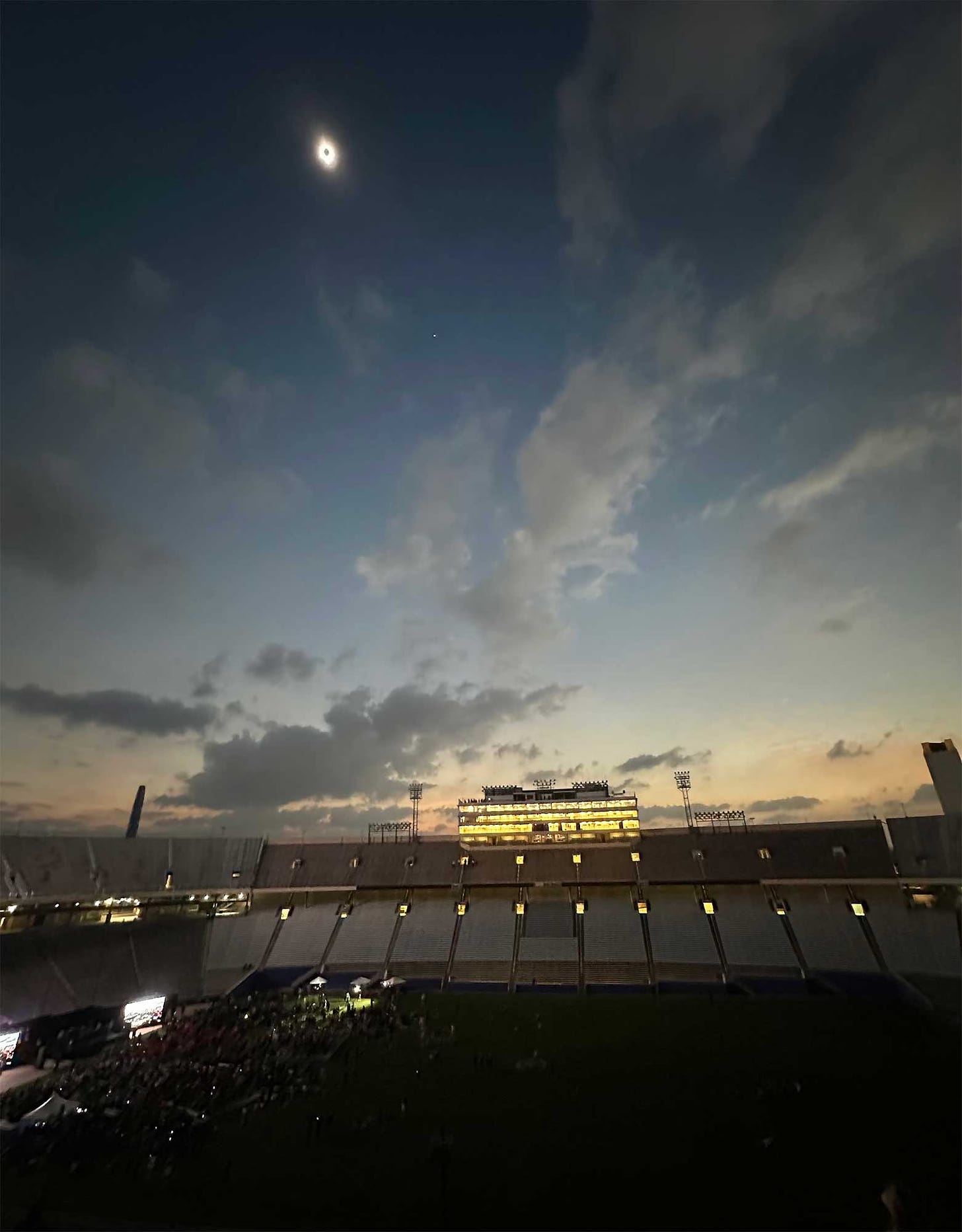 Eclipsed sun over stadium with stars visible in an early night like sky.