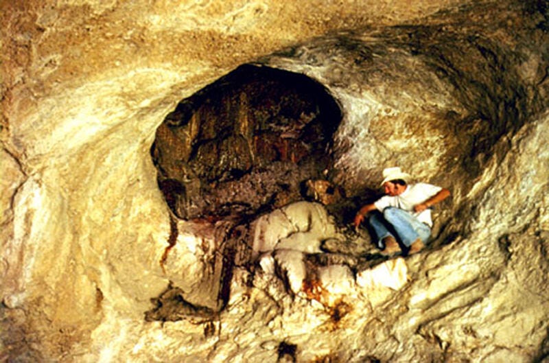 Man squatting in a cave next to packrat midden complex Man squatting in a cave next to packrat midden complex