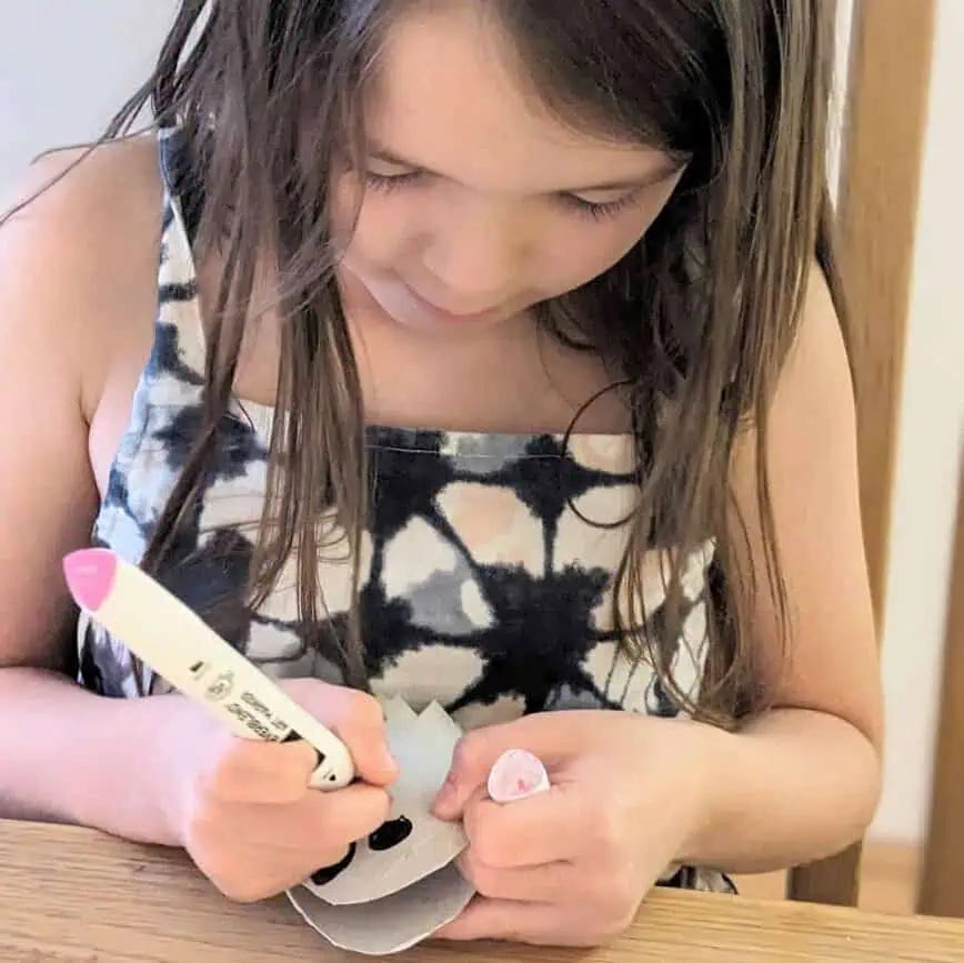 a 7 year old girl uses a pink marker to put the finishing touches to the cute ghost craft mobile 