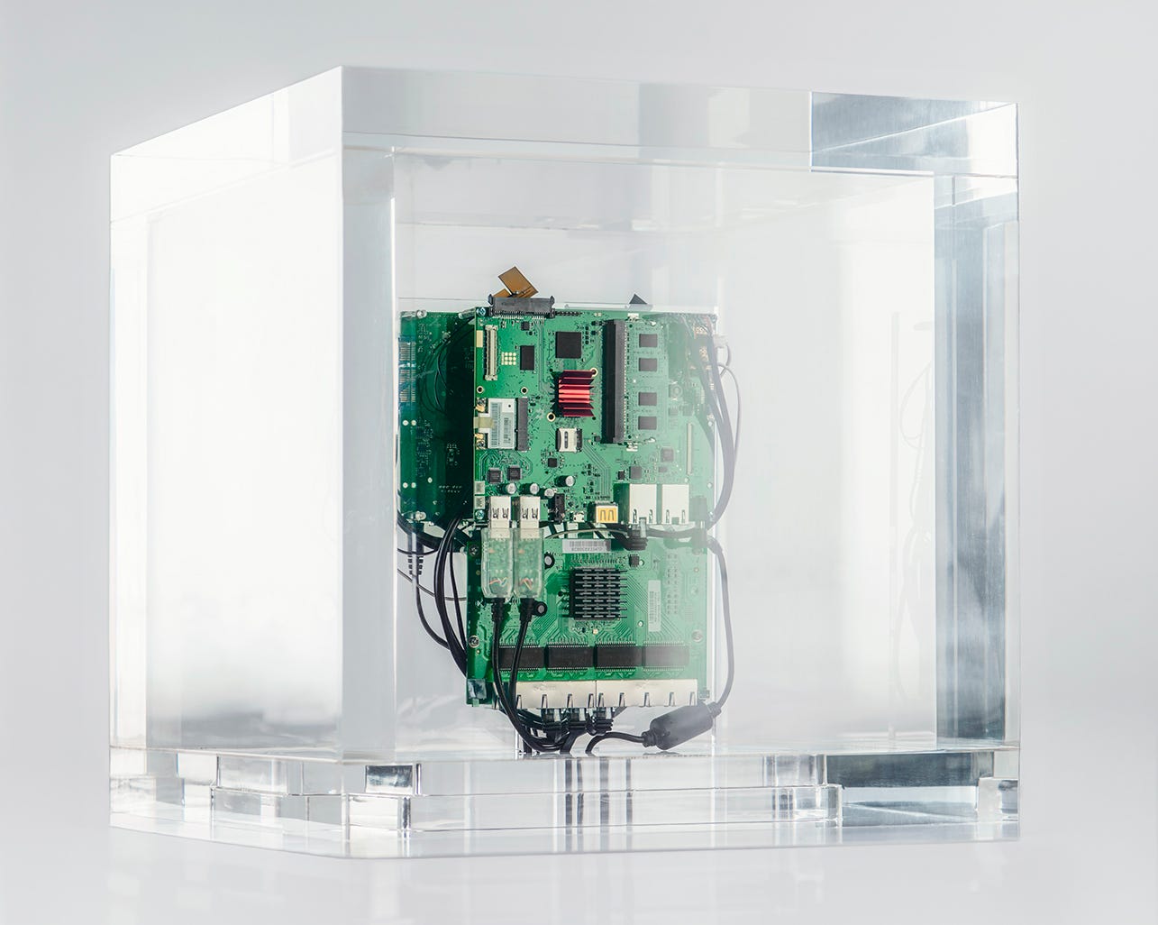 Picture of a live installation called Autonomy Cube by Trevor Paglen, comprising a clear perspex cube containing an electronic circuit board that is a working encrypted Wifi networking running through Tor.