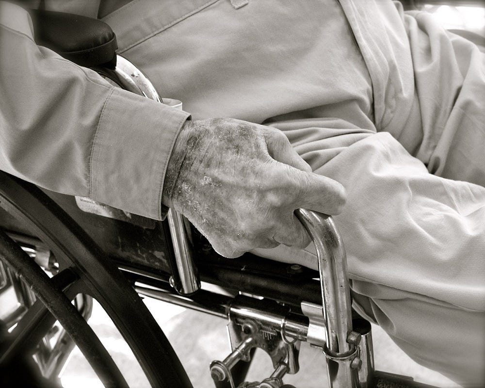 Close up of an elderly man in a wheelchair, his hands gripping the sides.