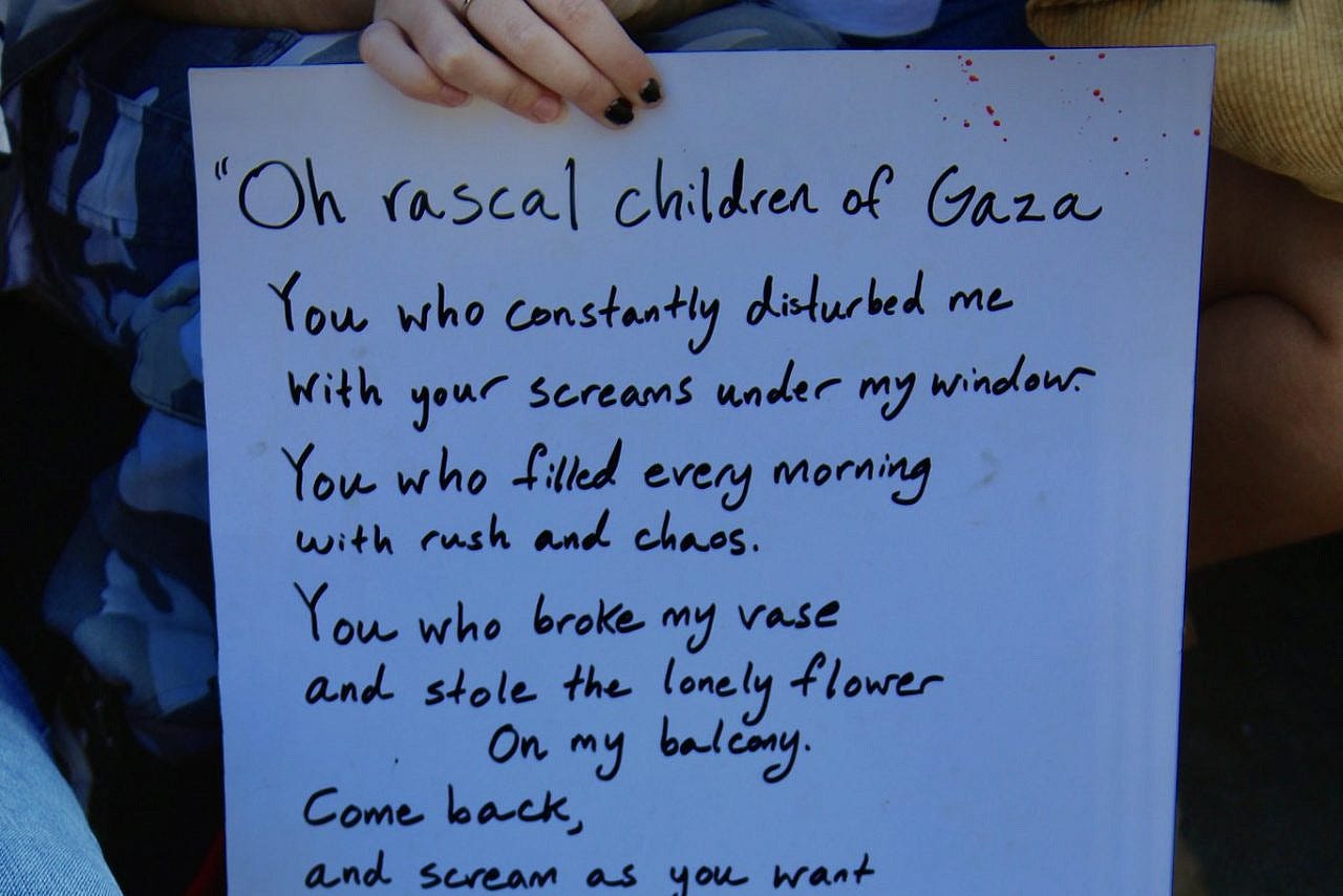 A student at the University of Oregon Gaza Solidarity Encampment holds a sign with a poem by Palestinian writer Khaled Juma, May 16, 2024. (Ian M./Flickr) A student at the University of Oregon Gaza Solidarity Encampment holds a sign with a poem by Palestinian writer Khaled Juma, May 16, 2024. (Ian M./Flickr)