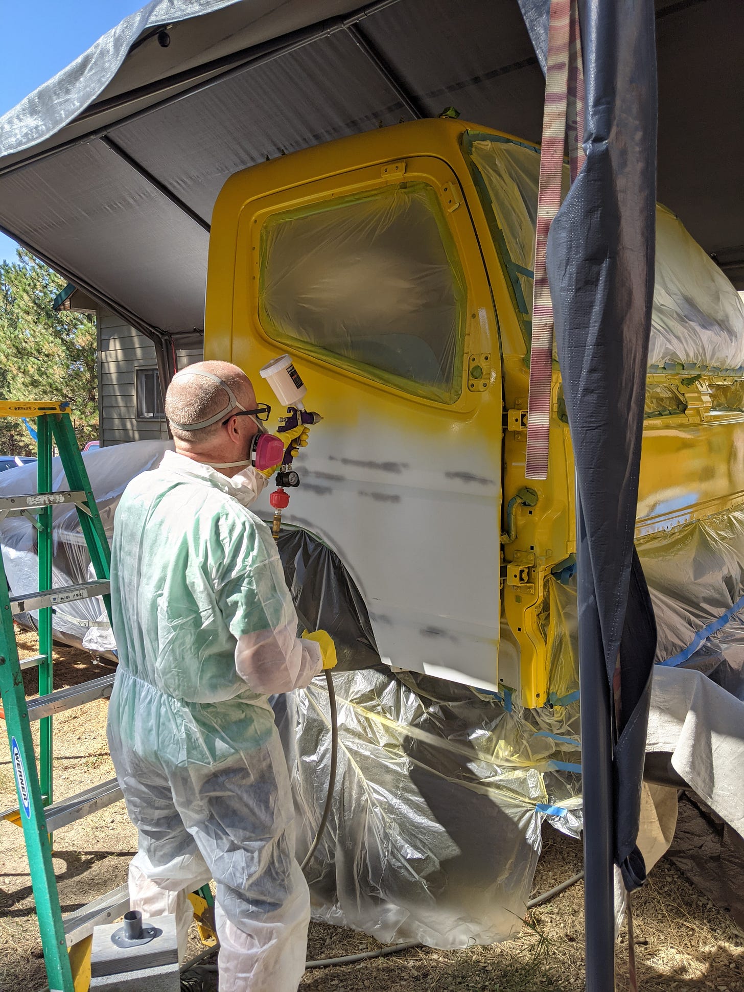 Andy in painter's coveralls and an air filtration mask, painting the white truck yellow