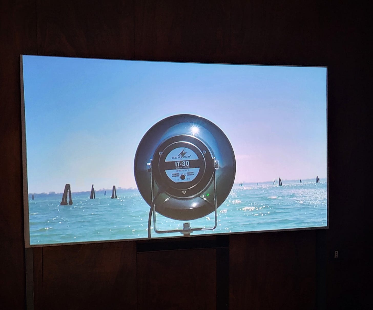 A projection shows a speaker turned to the sea against a bright blue sky.