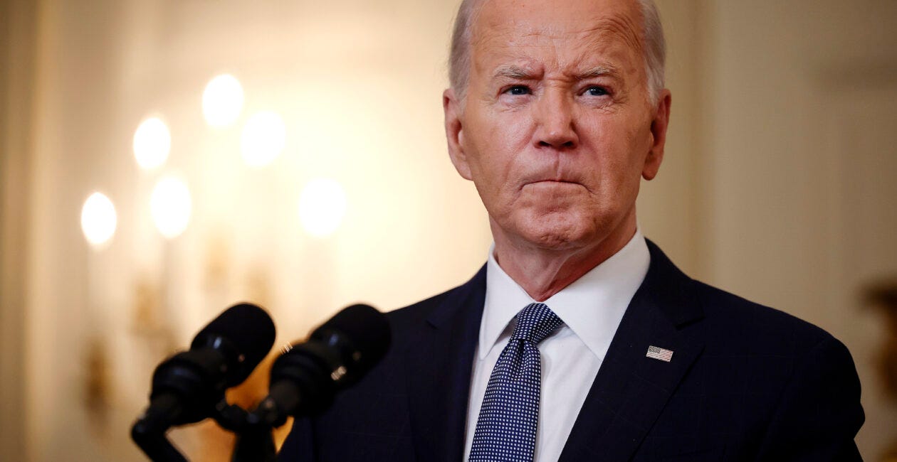 Joe Biden stands in front of a microphone wearing a suit and blue tie.