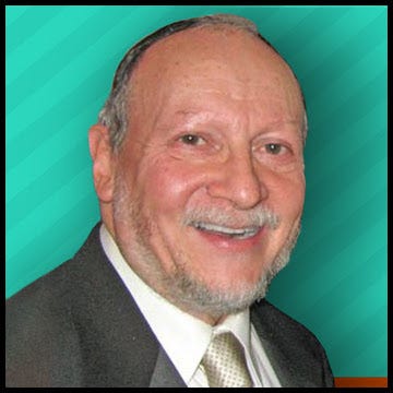 Rabbi Buchwald is a white-skinned man with a mustache and goatee. He wears a kippah and smiles at the camera
