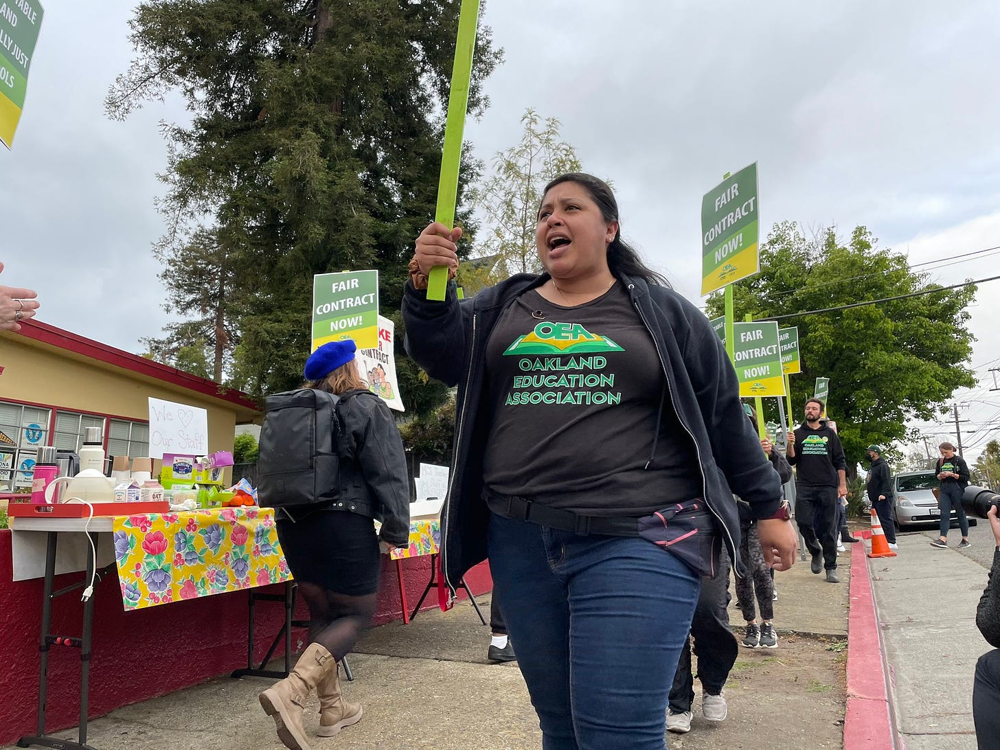 A person holds a sign on a picket line while wearing an Oakland Education Association shirt.