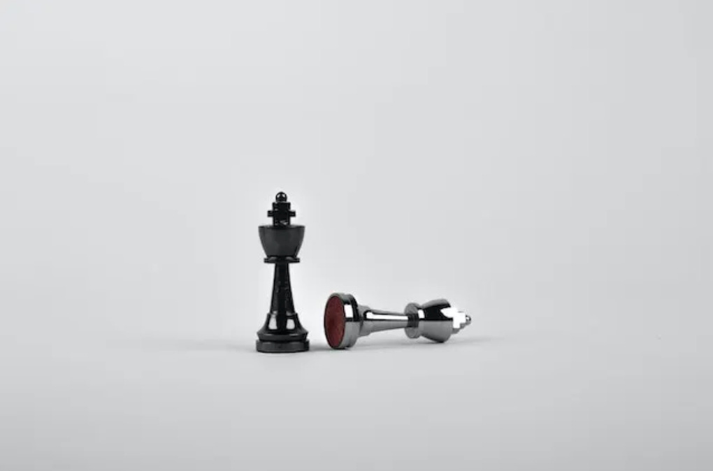 two king pieces from a chess set, on a white background. one is knocked over and the other is upright