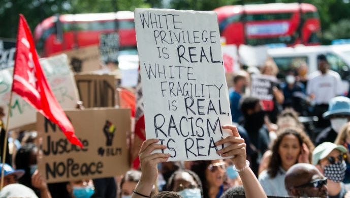 woman holding up sign that reads 'white privilege is real, white fragility is real, racism is real'