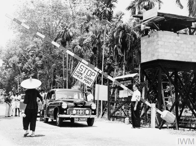 A member of the Malayan Home Guard mans a check point on the edge of a town. Such check points allowed the authorities to search vehicles and intercept food and supplies being smuggled out to the communist terrorists.