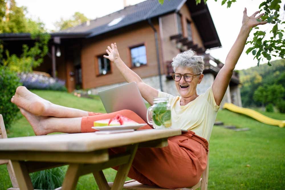 Energetic elder woman expressing excitement over a video call while sitting outdoors.