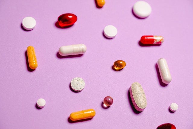 A photo of various pills and capsules, laid out on a pink background