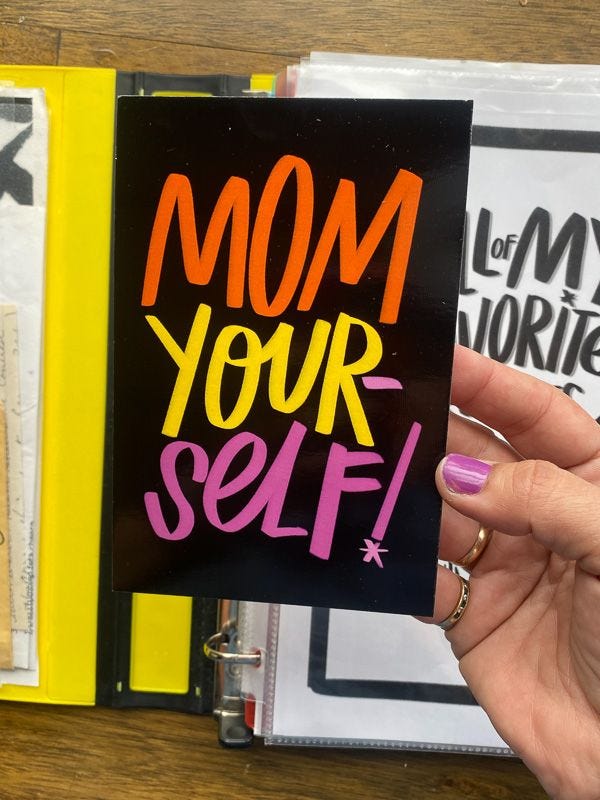 This may contain: a woman holding up a book with the words mom your self written on it in bright colors