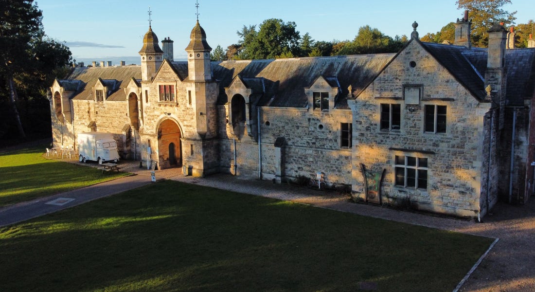 A pale brown brick castle building with a path leading up to it and green lawns