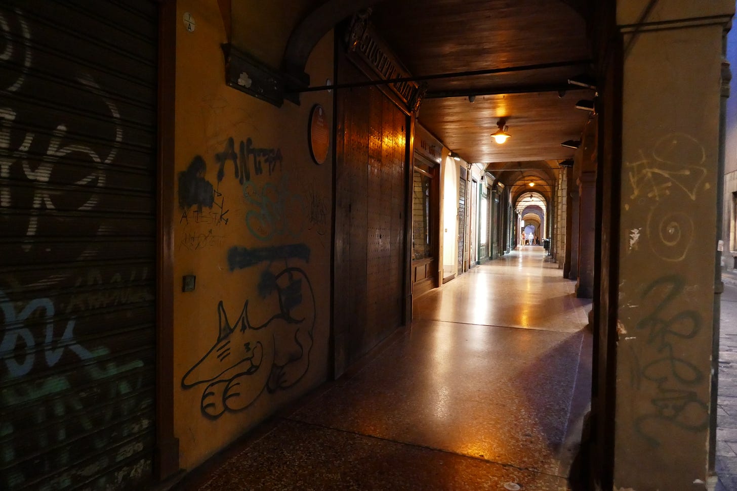 A dark and foreboding passageway in Bologna with grafitti of a rat and lamps in the distance