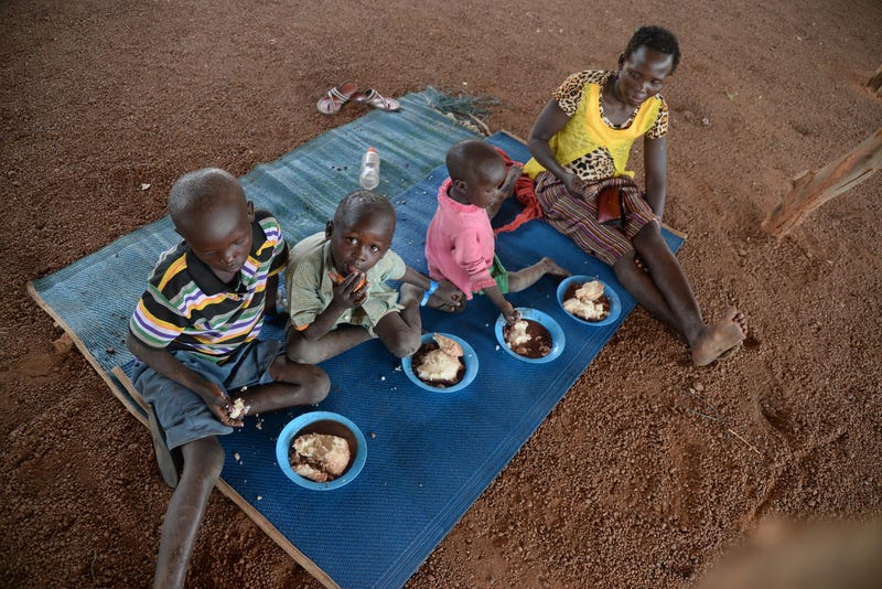 A woman and three children eat from four bowls while sitting on a blue blanket.