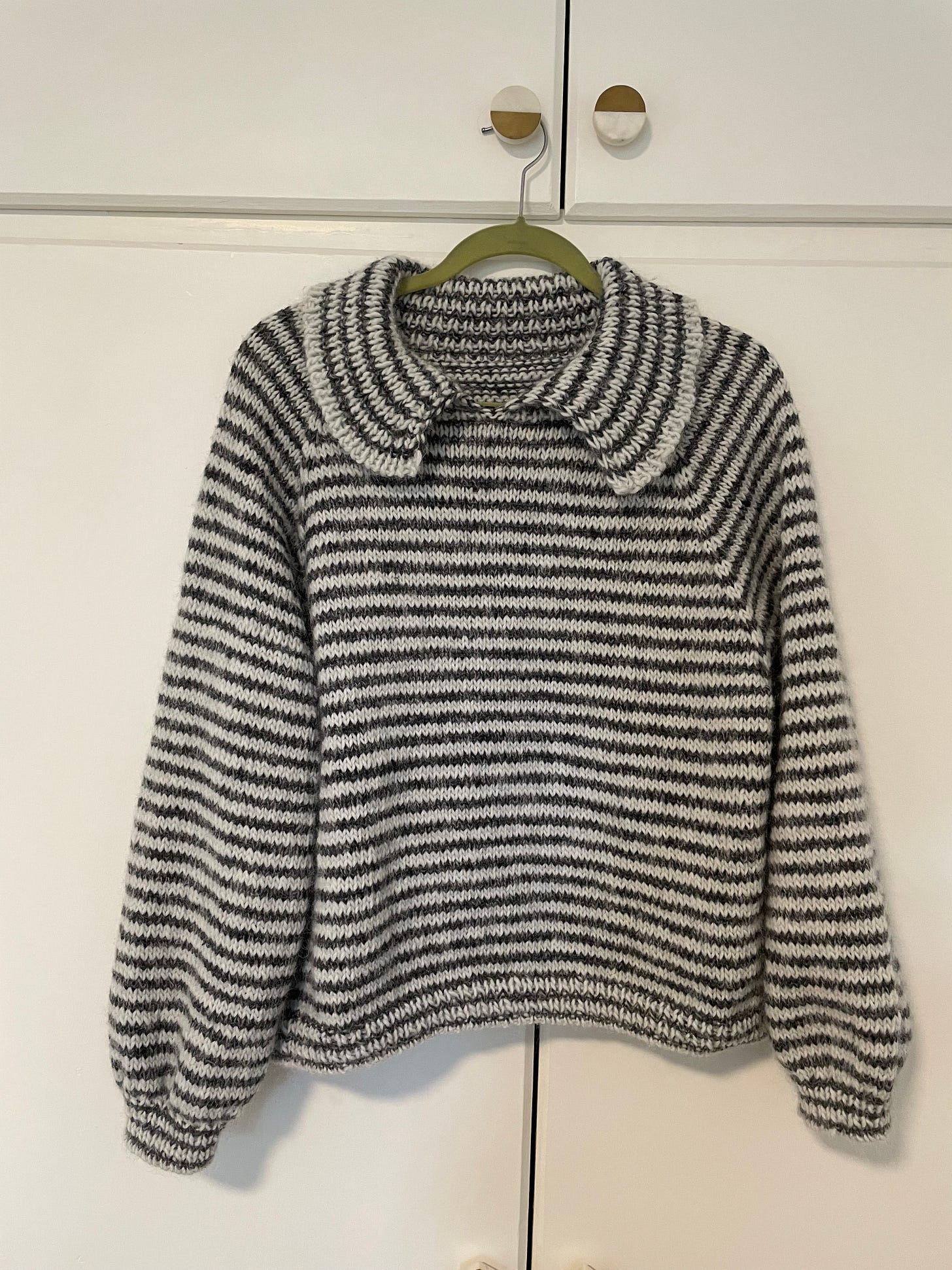 Handknit striped sweater hanging from hook.