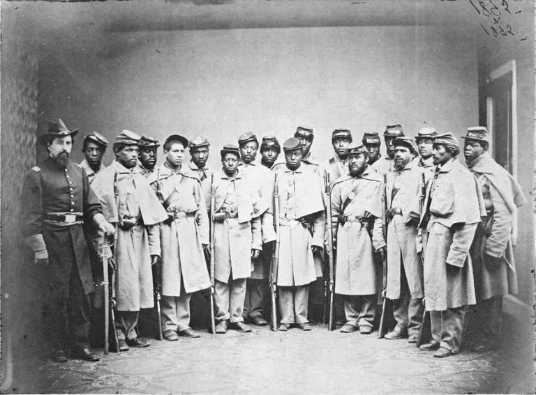 18 Black enlisted soldiers posed in semi-circle facing camera, their commanding officer standing to their right, interior studio sepia photo