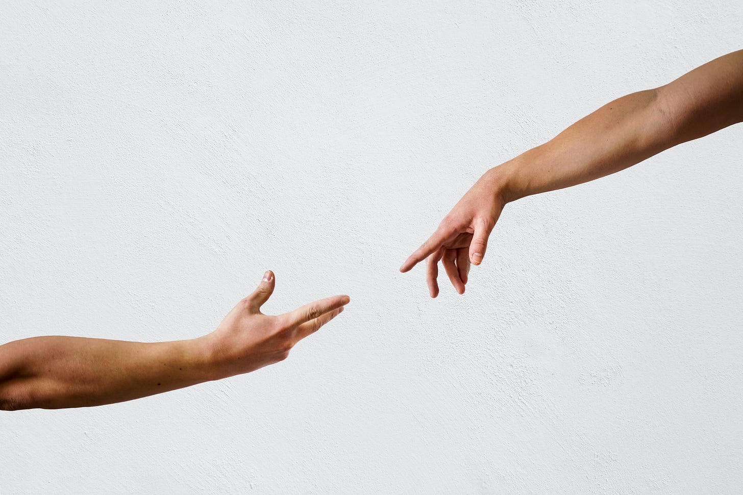 Two hands reaching towards one another. We can see the arms up to the elbow. Both arms are bare. Each person is Caucasian. The background is white.