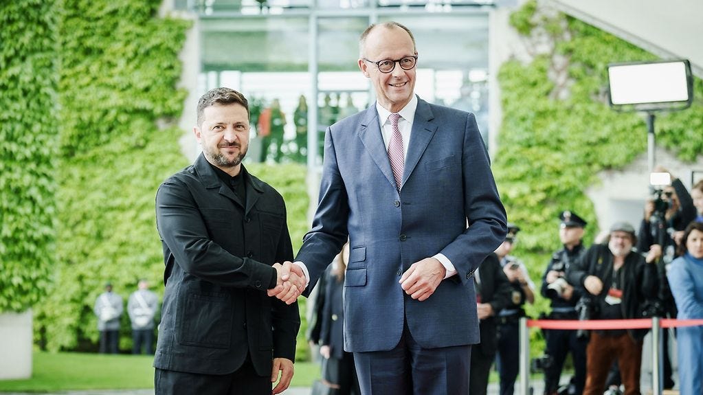 Bundeskanzler Merz begrüßt den ukrainischen Präsidenten Wolodymyr Selenskyj vor dem Bundeskanzleramt mit Handschlag. Im Hintergrund sind Medienschaffende zu sehen.