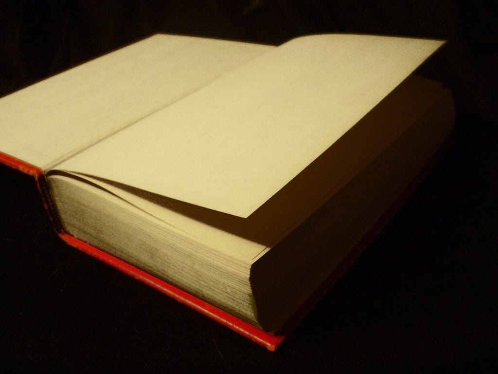 A blank book with a red cover, opened to its first page. "blank book opene" by Jo Naylor is licensed under CC BY 2.0. 