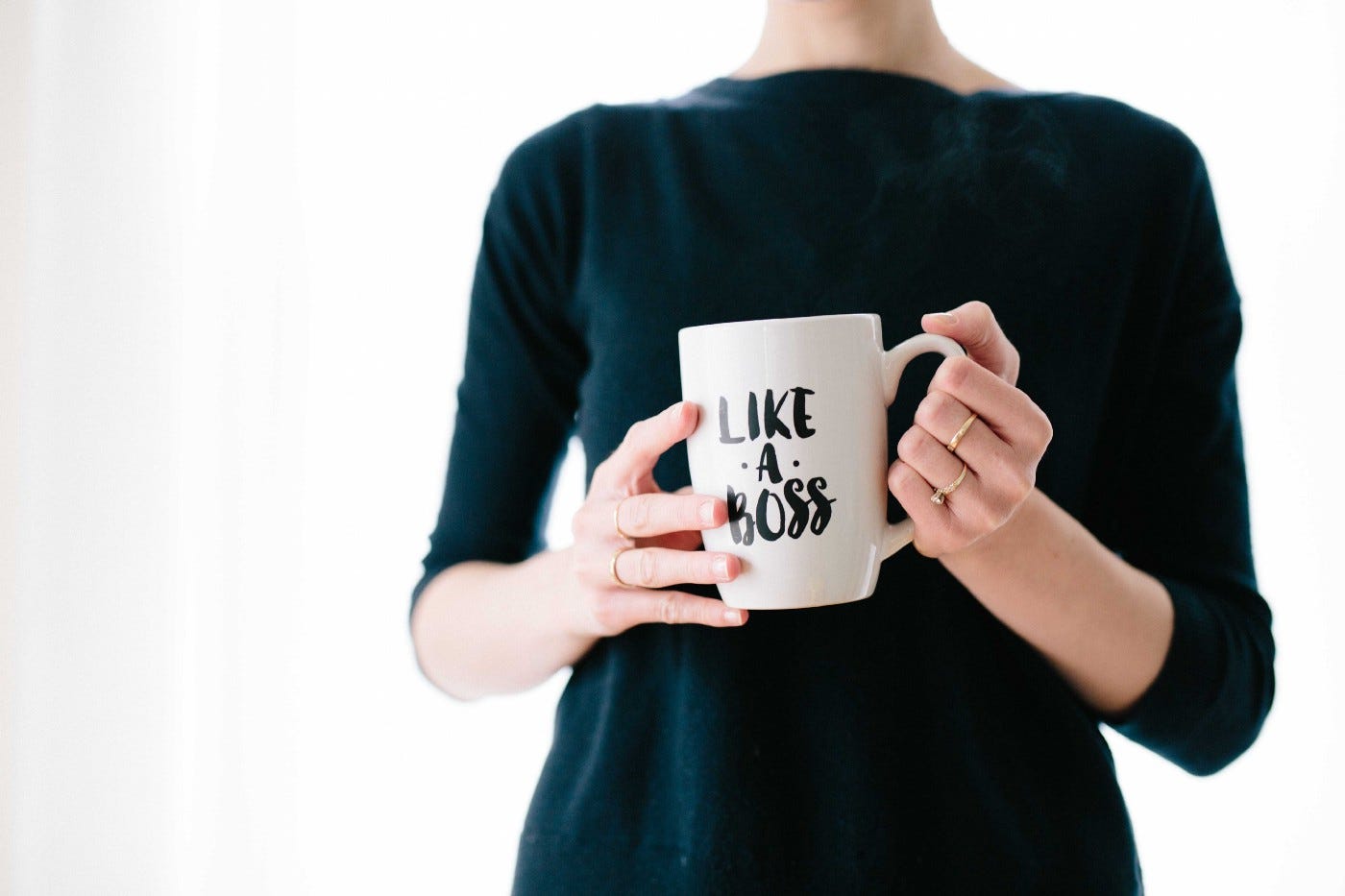 Picture of a woman with a black jumper holding a coffee cup that reads “Like a Boss”