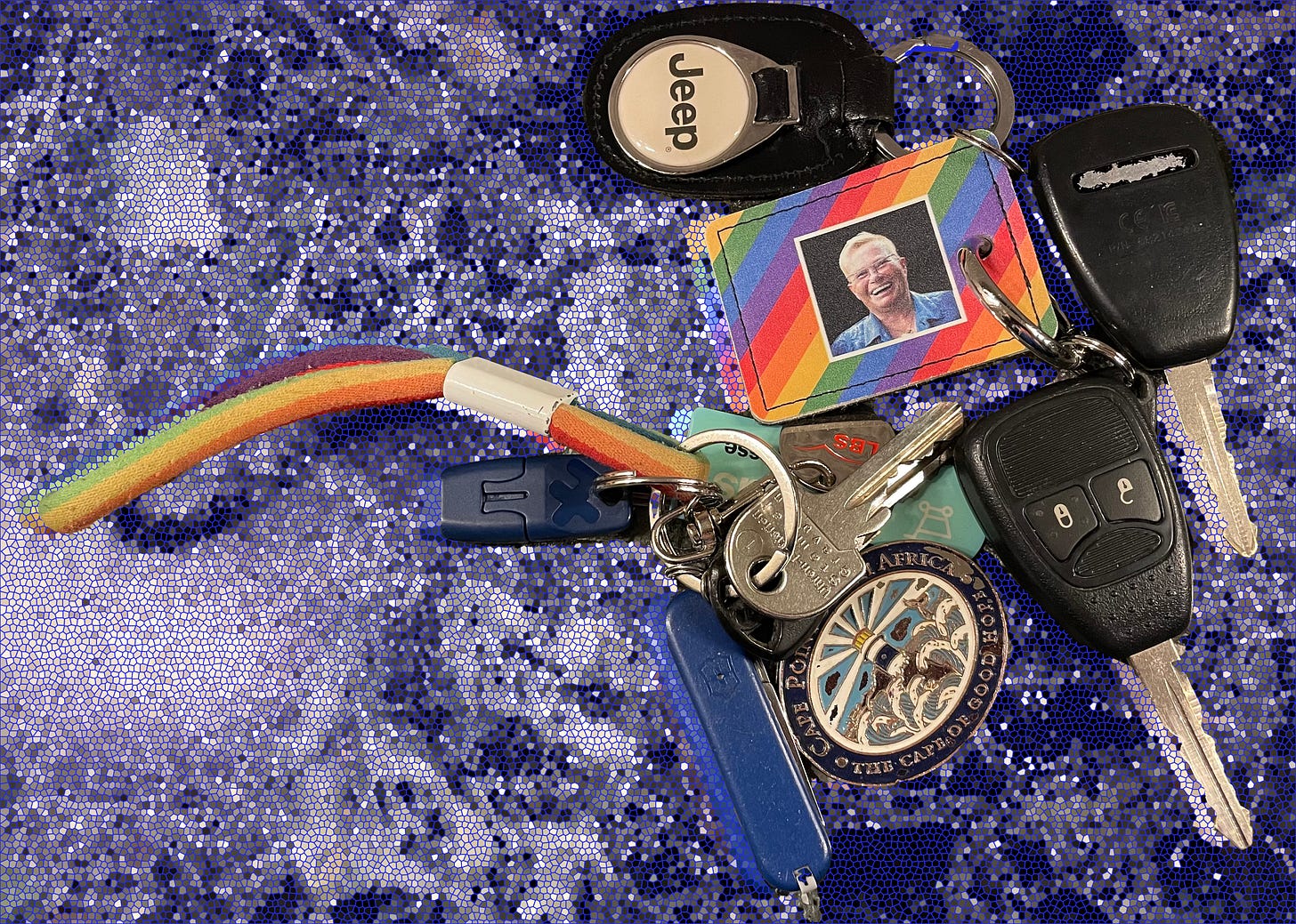 A large collection of keys on a dark mosaic-patterned background, featuring car keys, an antique skeleton key, a rainbow keychain with a photo, a Swiss Army knife, and various house keys.