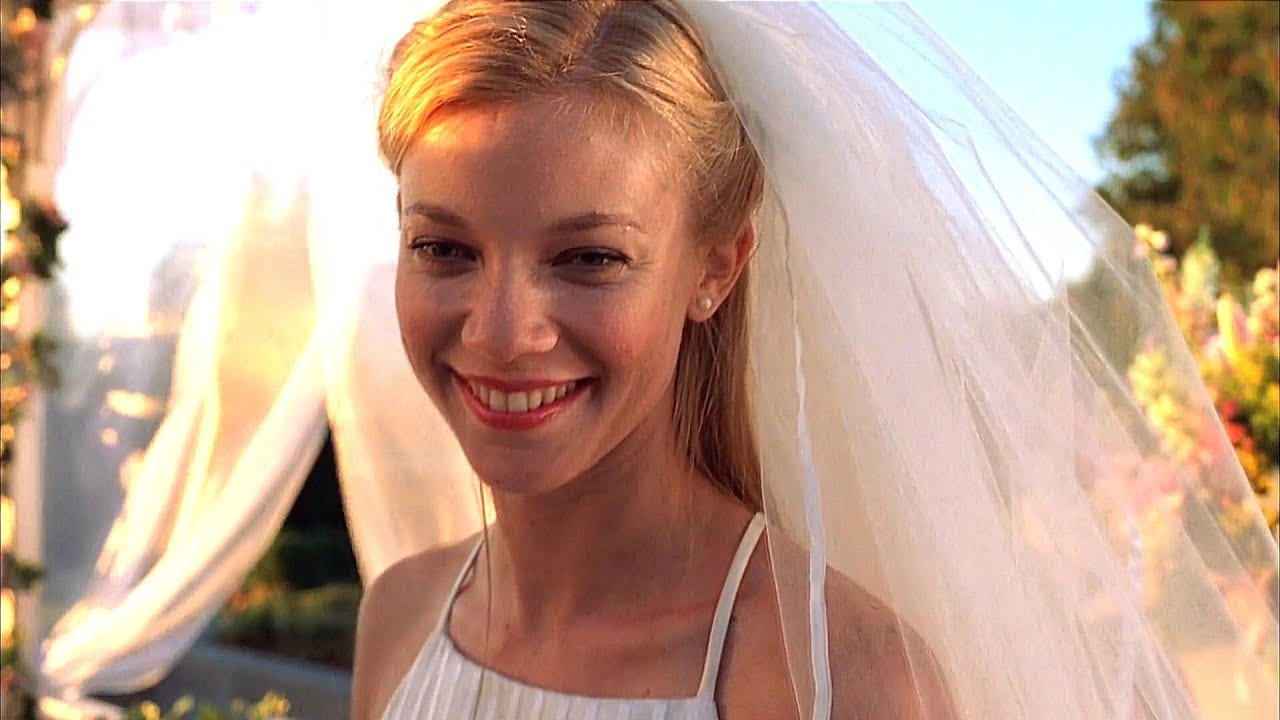 Movie still from The Butterfly Effect. Amy Smart smiles in a wedding dress and veil, the sun setting behind her.